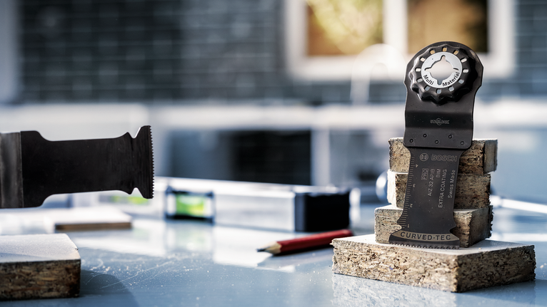 Oscillating multi-tool blade stands upright on stacked cork blocks beside a pencil and level.