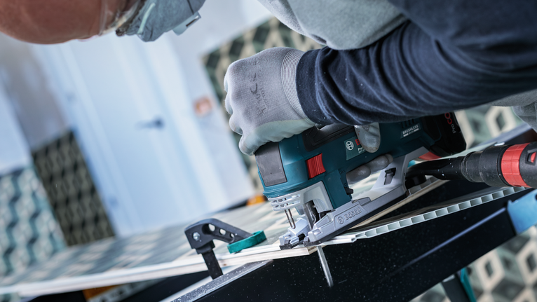 Person wearing safety equipment cuts tile using an electric jigsaw.