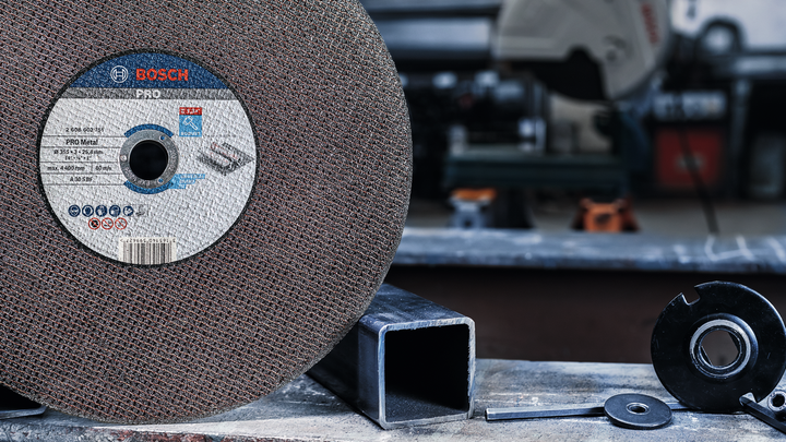 Large abrasive grinding wheel positioned beside a metal square tube on a workshop table.