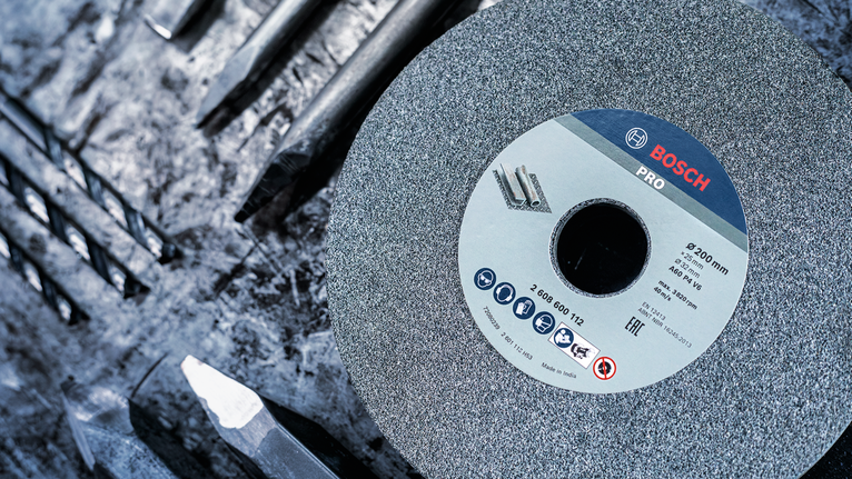 Grinding disc on a workbench with various drill bits arranged nearby.