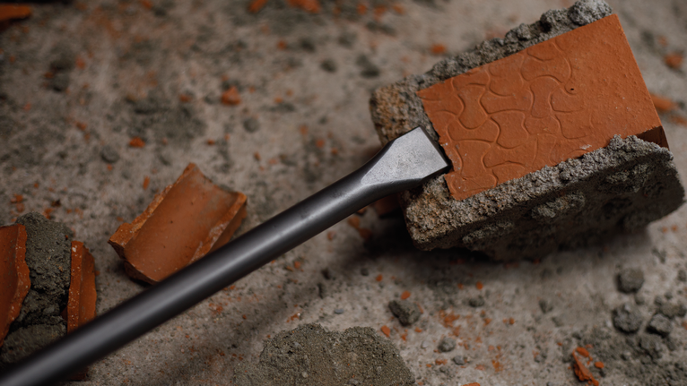 Chisel breaking a brick block on a concrete surface.