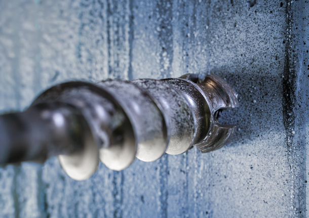 A close-up of a masonry drill bit boring into a concrete wall.