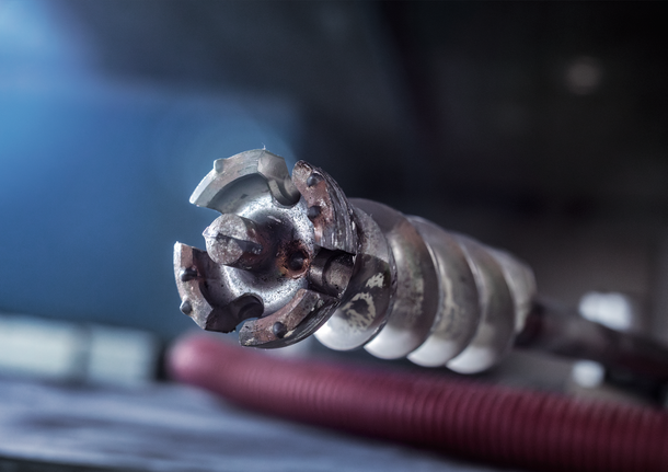Close-up of a heavy-duty drill bit with visible wear, resting on a workbench.