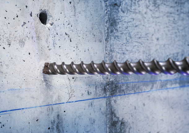 Large drill bit boring into a concrete wall with blue guideline markings.