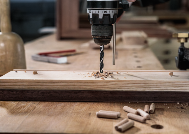Person drilling a hole into a wooden plank on a workbench.