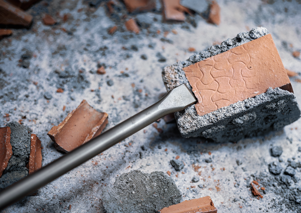 Chisel bit breaking a brick surrounded by scattered rubble.