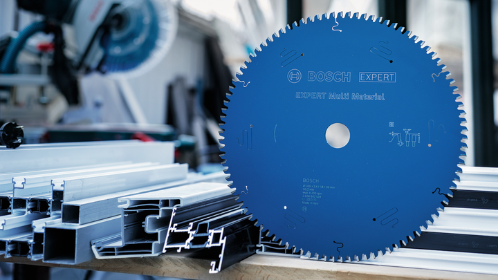 Large blue circular saw blade on a workbench beside stacked metal profiles.