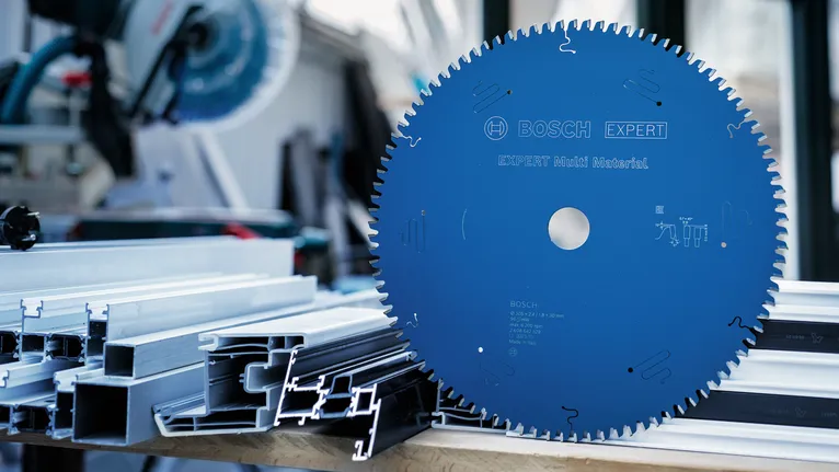 Large blue circular saw blade on a workbench beside stacked metal profiles.