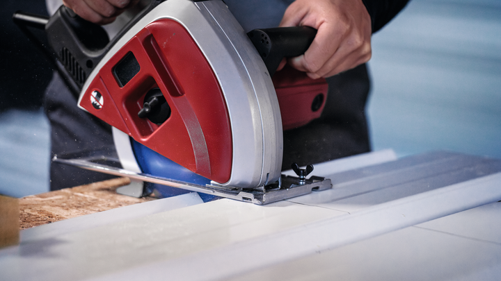 Person using a circular saw to cut a board along a metal guide.