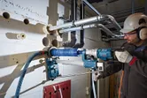 Une personne portant un équipement de sécurité utilise un support de perceuse pour percer de grands trous dans un mur en béton.