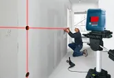 Une personne portant un équipement de sécurité utilise un outil de nivellement laser pour marquer des lignes sur un mur.