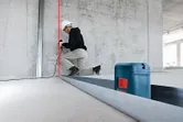 Une personne portant un équipement de sécurité aligne une ossature métallique à l’aide d’un outil de nivellement laser.