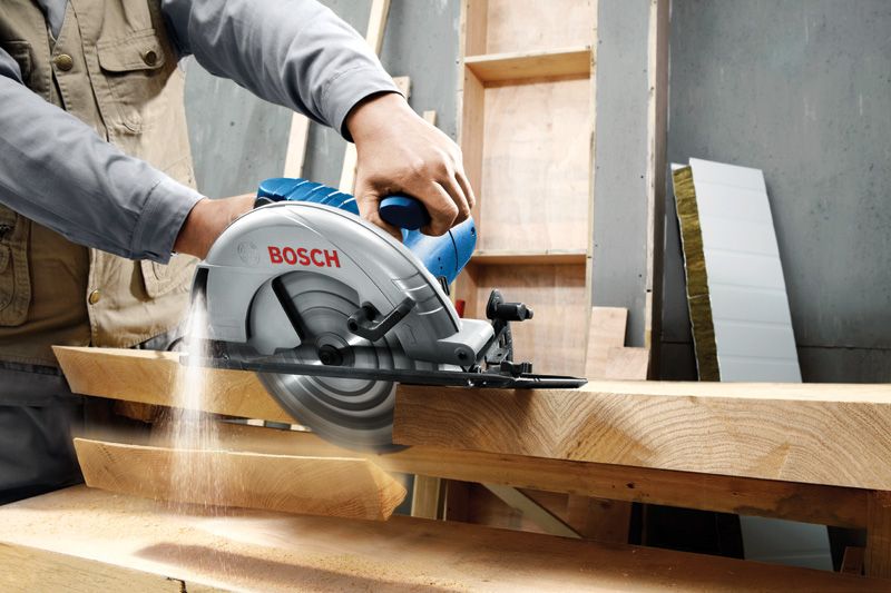 Une personne guide une scie circulaire à travers d'épaisses planches de bois dans un atelier.