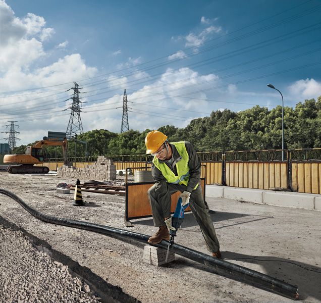 Une personne portant un équipement de sécurité utilise une scie alternative pour couper un tuyau sur un chantier de construction.