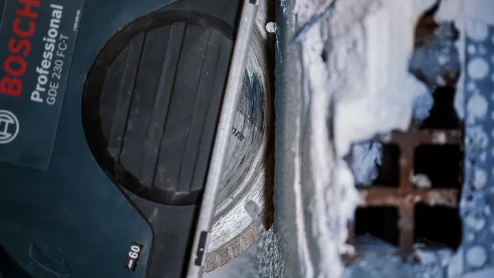 Un outil de coupe avec une lame diamantée tranche le béton à proximité d'une grille métallique.