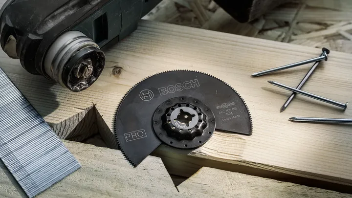 Accessoire de lame de scie circulaire placé sur une planche de bois à côté de clous et d'un outil électrique.