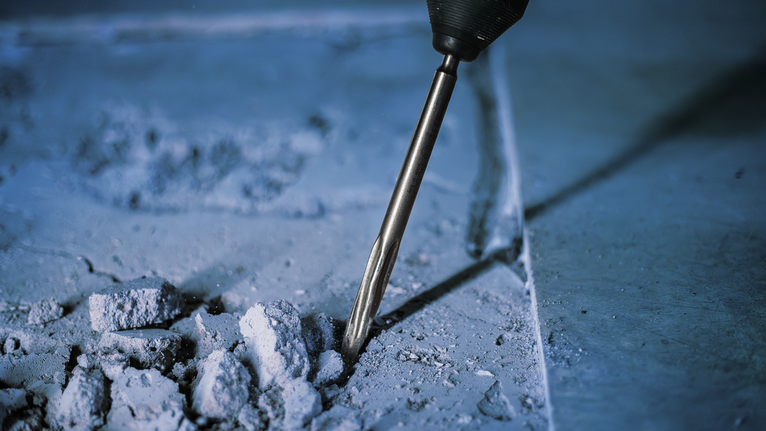 Un marteau perforateur brise du béton, créant des gravats sur une surface de construction.