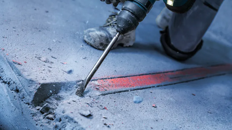 Une personne portant un équipement de sécurité utilise un marteau rotatif pour briser un sol en béton.