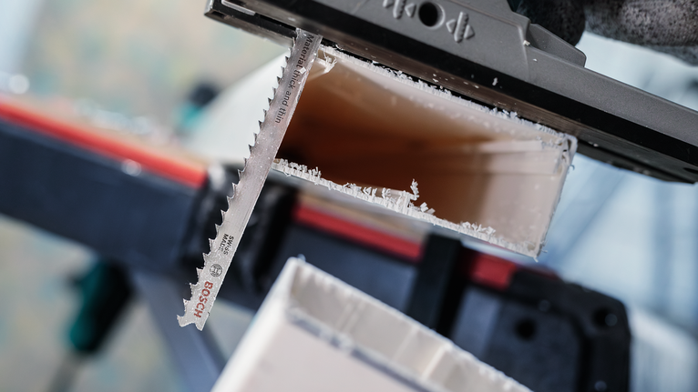 Une lame de scie sauteuse coupe un tuyau en plastique tandis qu'un travailleur porte un équipement de sécurité.