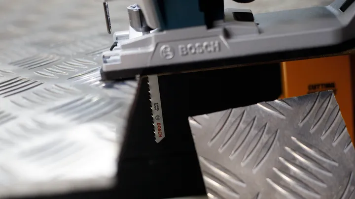 Découpe à la scie sauteuse d'une plaque métallique striée.