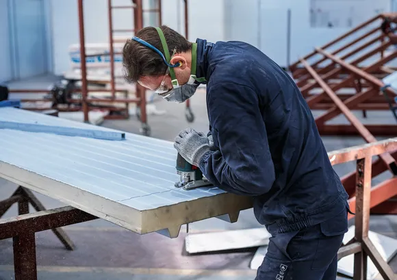 Une personne portant un équipement de sécurité utilise une scie sauteuse pour découper des rainures dans un panneau isolé.
