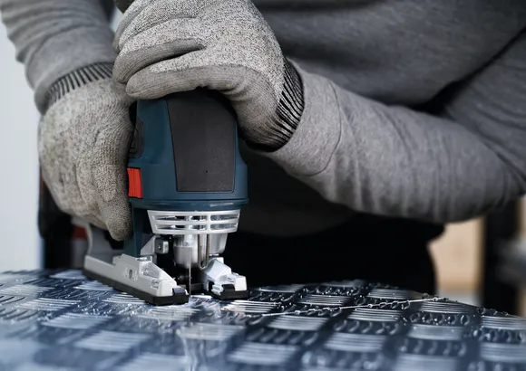 Une personne portant un équipement de sécurité utilise une scie sauteuse pour couper du métal à motifs.