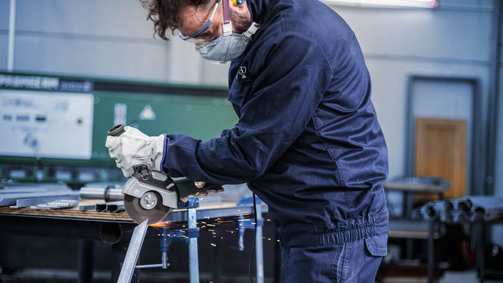 Une personne portant un équipement de sécurité utilise une meuleuse d’angle pour couper du métal, produisant des étincelles.
