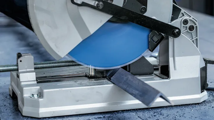 Une scie à métaux coupe une barre d'acier sur une table d'atelier.