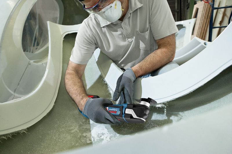 Güvenlik ekipmanı takan bir kişi, kablosuz çok amaçlı aletle fiberglas kesiyor.