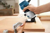Bir kişi ahşap bir levhanın kenarını şekillendirmek için avuç içi frezesini kullanır.
