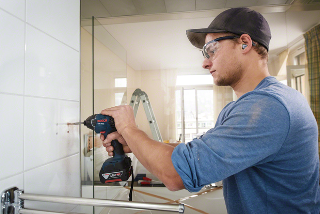 Güvenlik ekipmanı takan bir işçi fayanslı banyo duvarını deliyor.