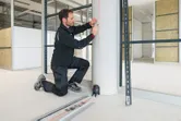 Güvenlik ekipmanı giyen bir kişi, lazerli seviyeleme aleti kullanarak bir sütun üzerinde dikey bir çizgi işaretliyor.