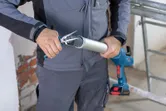Güvenlik ekipmanı takan bir kişi, kablosuz derz dolgu tabancası için derz dolgu borusunun ucunu kesiyor.