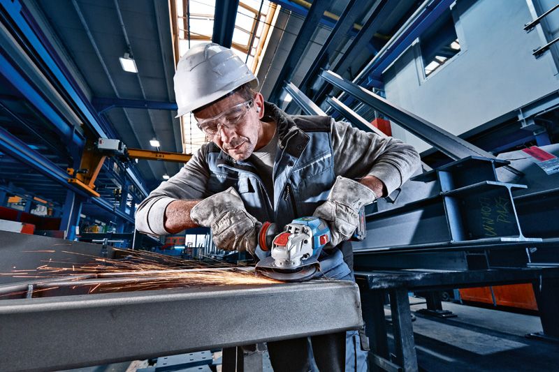 Güvenlik ekipmanı giyen bir kişi, akülü açılı taşlama makinesiyle metal taşlıyor ve kıvılcımlar çıkıyor.