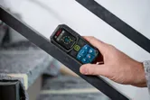 Bir kişi lazer ölçüm cihazı kullanarak metal bir korkuluğun açısını kontrol ediyor.