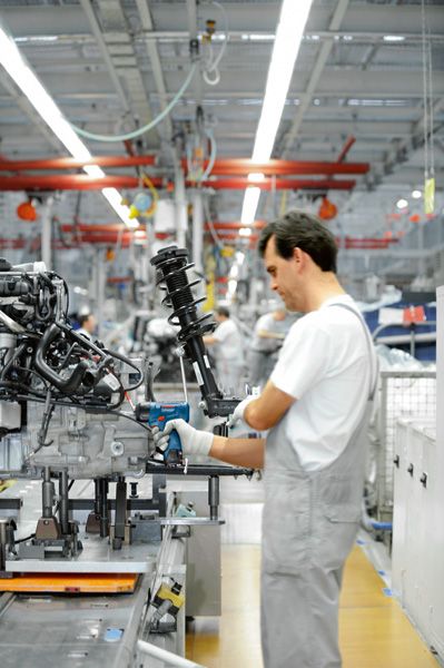 Güvenlik ekipmanı takan kişi, bir fabrika hattındaki makineleri monte etmek için elektrikli bir alet kullanıyor.