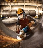 Güvenlik ekipmanı takan bir kişi açılı taşlama makinesiyle büyük bir metal boruyu taşlıyor.