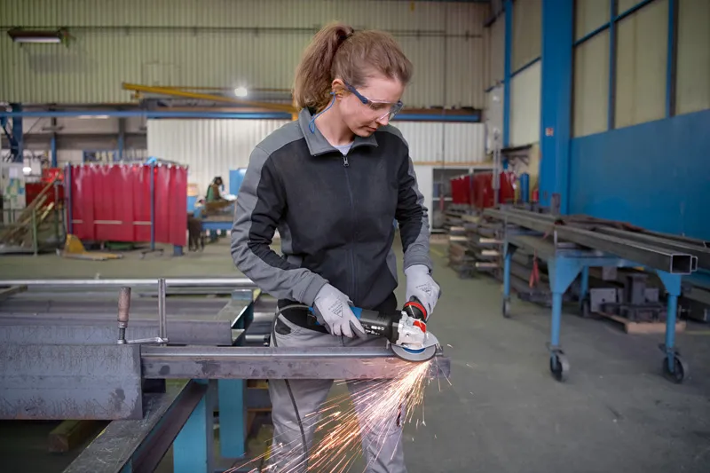Güvenlik ekipmanı takan bir kişi açılı taşlama makinesi kullanarak metal keserken kıvılcımlar çıkıyor.