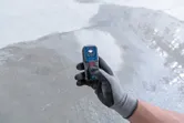 Güvenlik ekipmanı giymiş bir kişi, beton zeminde lazer ölçüm cihazı kullanıyor.