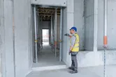 Güvenlik ekipmanı giyen bir kişi, beton bir binanın içindeki mesafeyi ölçmek için lazer ölçüm cihazı kullanıyor.