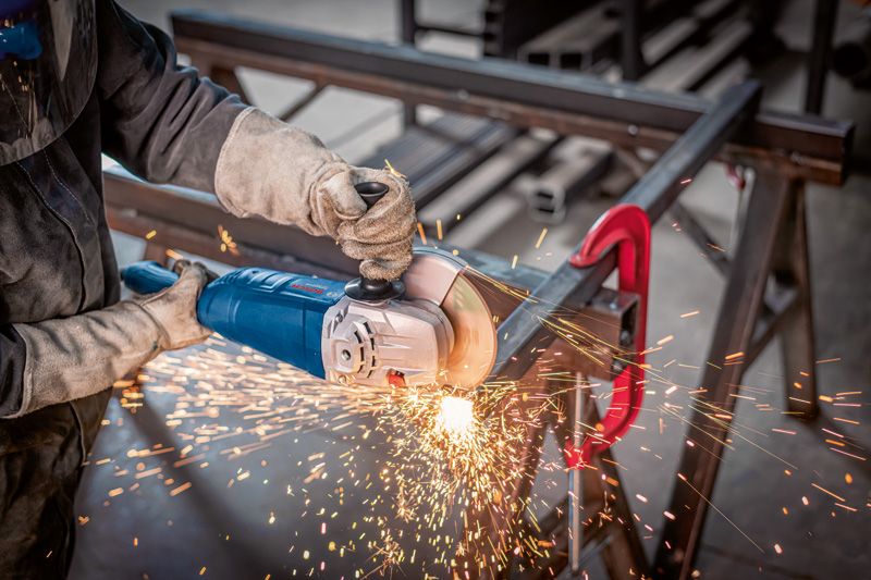 Güvenlik ekipmanı takan bir kişi açılı taşlama makinesiyle metal öğütüyor ve kıvılcımlar çıkıyor.