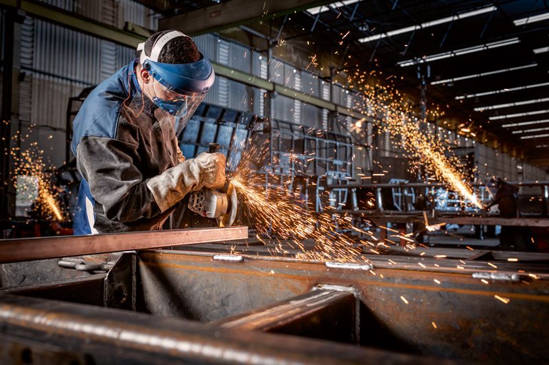 Güvenlik ekipmanı takan bir kişi açılı taşlama makinesiyle metal keserken kıvılcımlar çıkıyor.