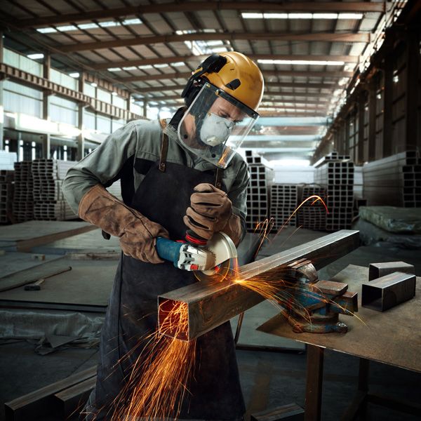 Güvenlik ekipmanı takmış bir kişi açılı taşlama makinesiyle metal bir kirişi taşlıyor, kıvılcımlar çıkıyor.