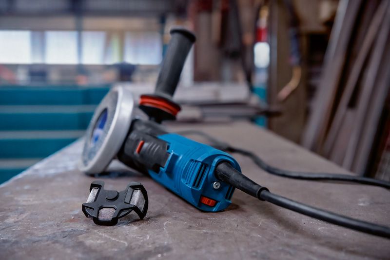 Elektrikli açılı taşlama makinesi, küçük bir toz filtresinin yanında bir çalışma tezgahının üzerinde duruyor.