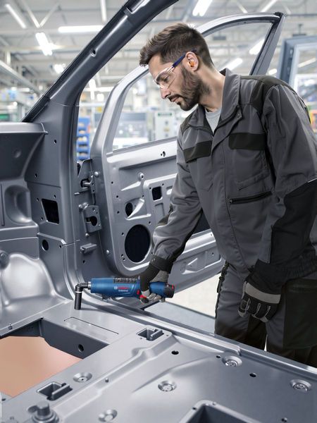 Güvenlik ekipmanı takan bir kişi, endüstriyel bir ortamda bir araç şasisinde elektrikli alet kullanıyor.