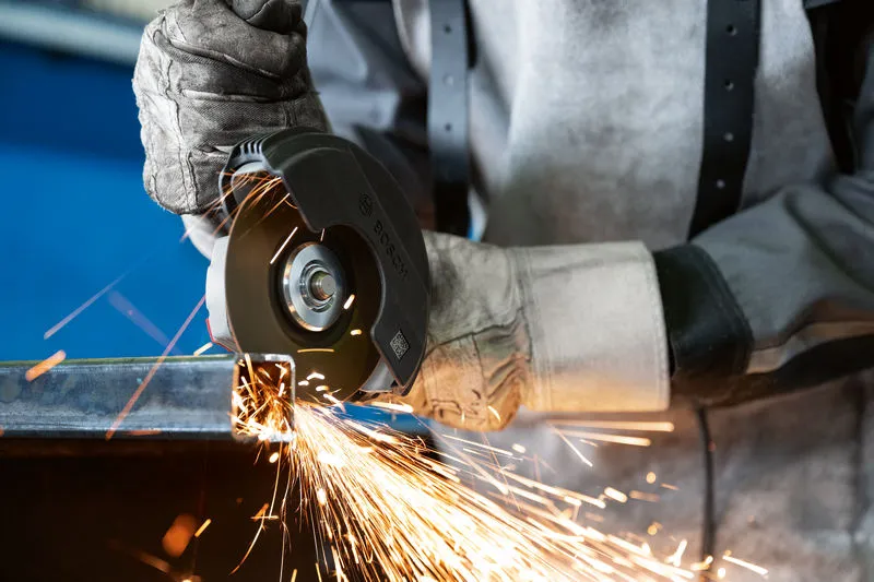 Güvenlik ekipmanı takan bir kişi açılı taşlama makinesiyle metal keserken kıvılcım çıkıyor.