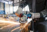 Güvenlik ekipmanı takan bir kişi açılı taşlama makinesi kullanarak kıvılcımlar saçarak metal öğütüyor.