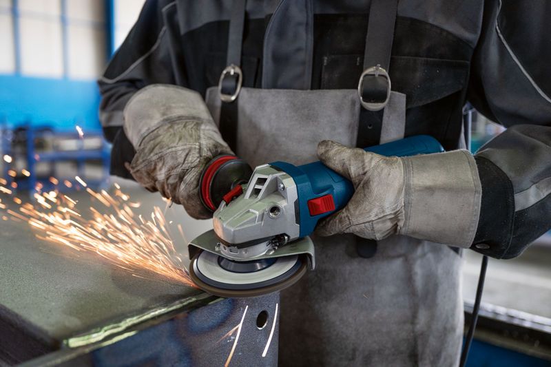 Güvenlik ekipmanı takmış bir kişi açılı taşlama makinesiyle metal öğütüyor, kıvılcımlar çıkıyor.