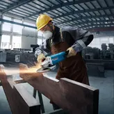 Güvenlik ekipmanı takan bir kişi elektrikli aletle metal öğütüyor, kıvılcımlar çıkıyor.