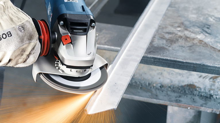 Güvenlik ekipmanı takan işçi açılı taşlama makinesiyle metal bir çubuğu taşlıyor.